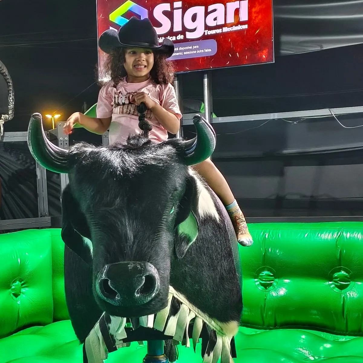 Menina pequena de chapéu montando o 9 Pulos, com o painel Sigari ao fundo